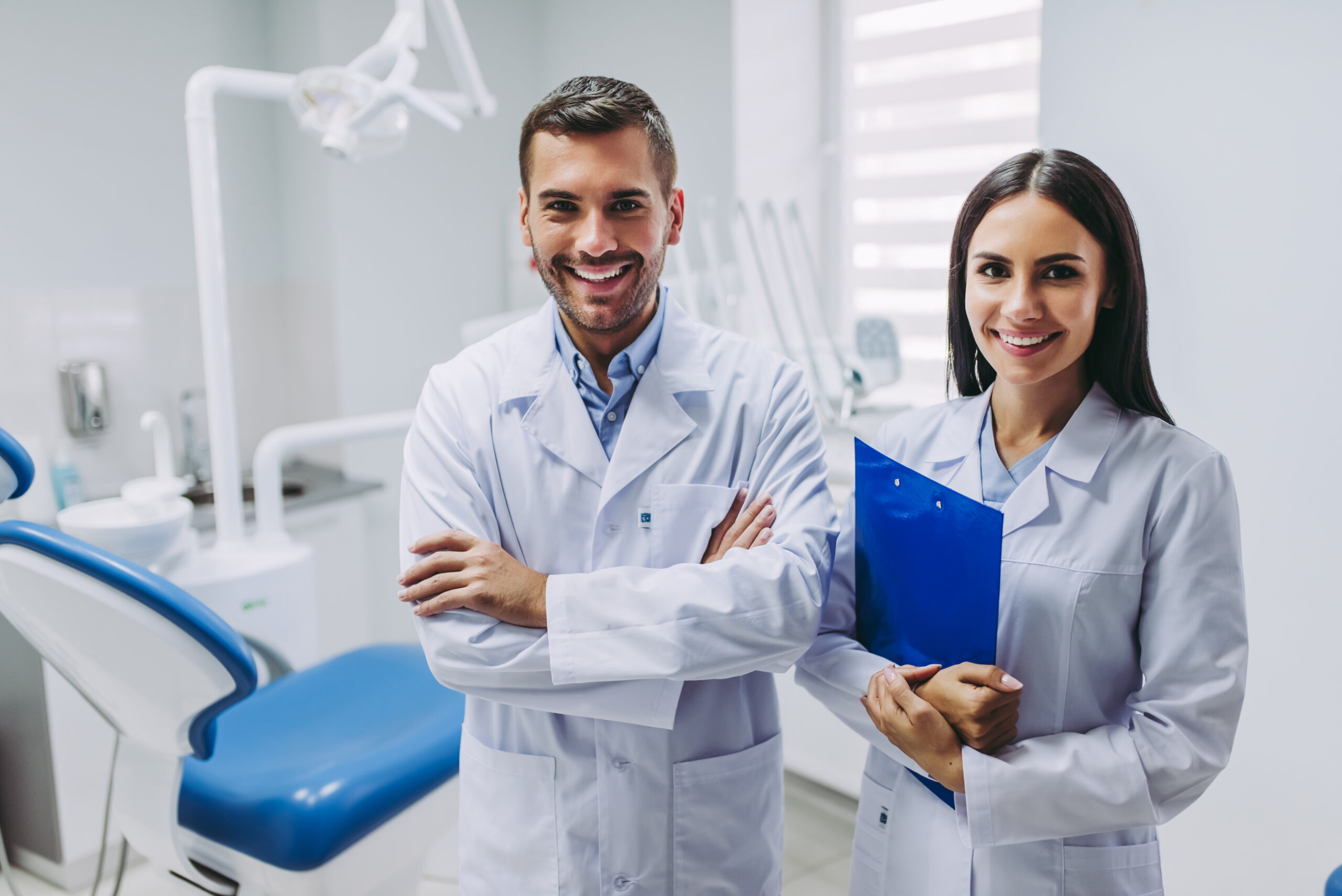 portrait of two smiling doctors looking at the camera standing at workplace in modern dental clinic